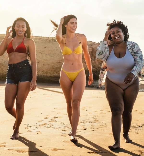 3 diverse woman in the beach with different body size and skin color